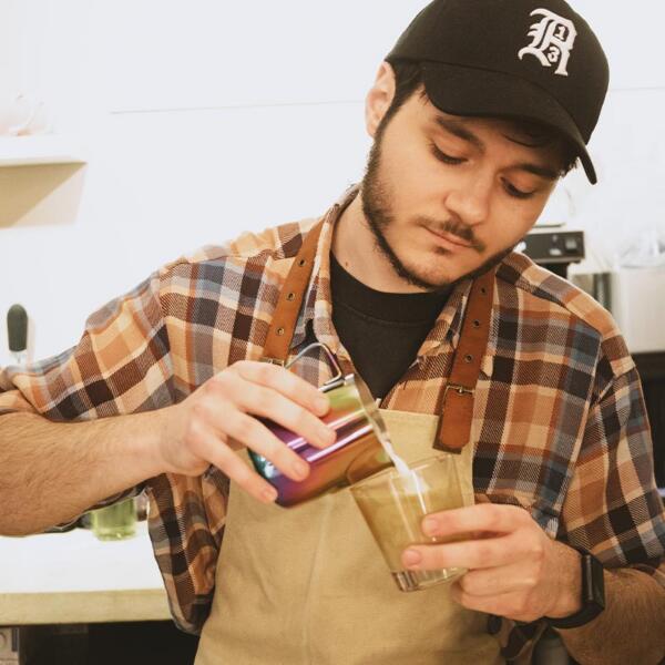 Young male barista pouring a coffee